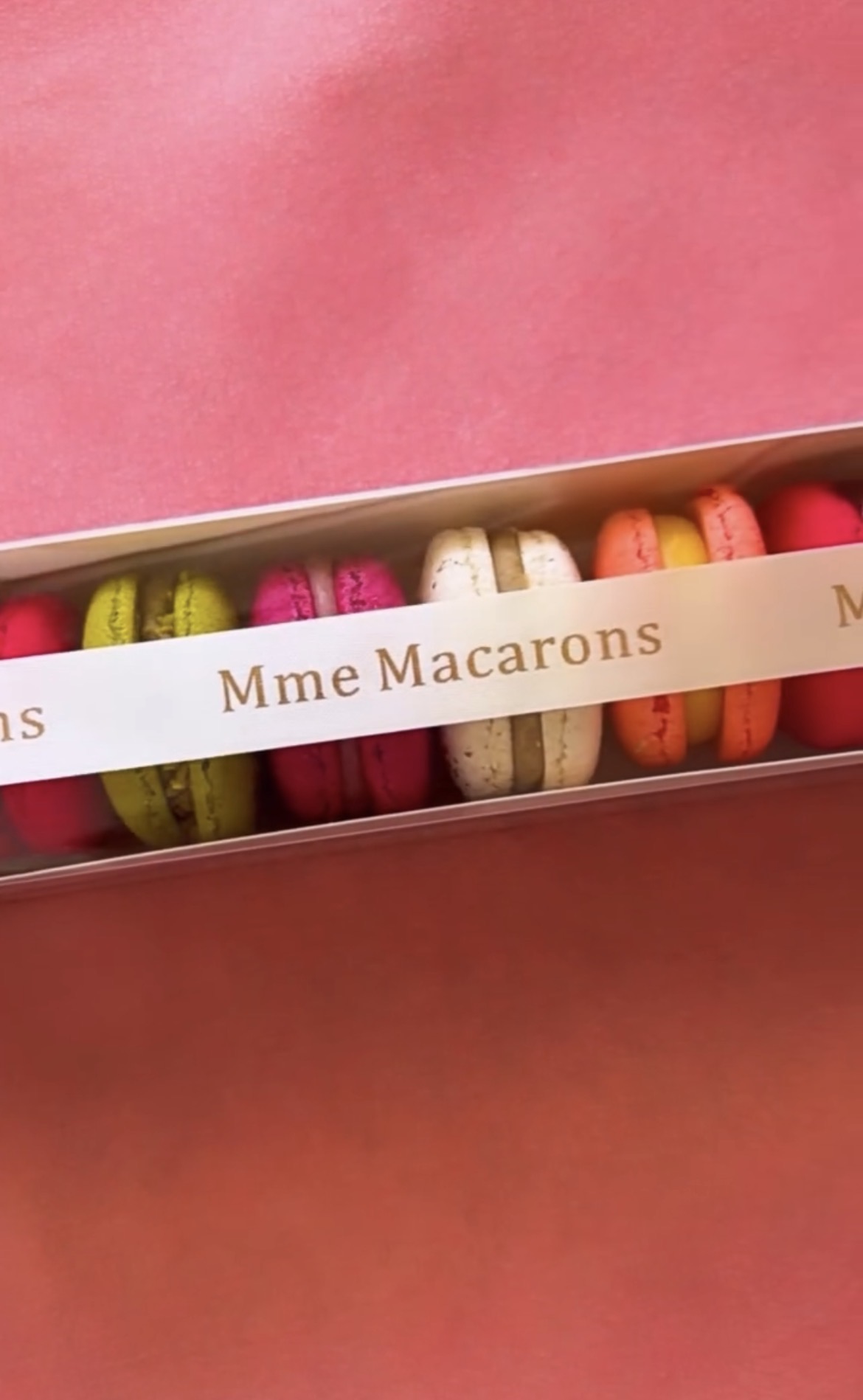 Coffret de macarons Mme Macarons fermé par un ruban doré, sur fond rose