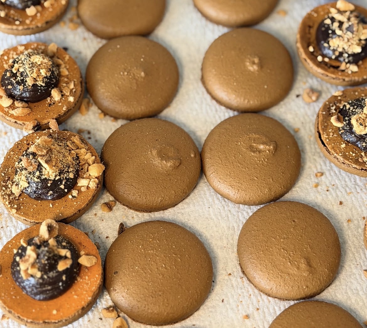 Coques de macarons chocolat garnies de ganache et d'éclats de noisette dans l'atelier
