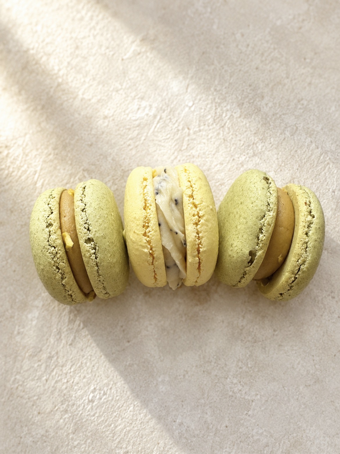 Trois macarons artisanaux pistache et caramel posés sur une pierre beige