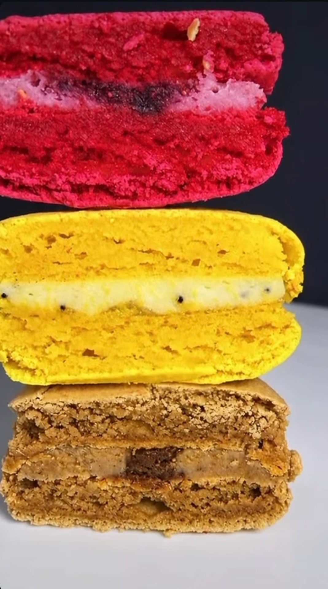 Trois macarons coupés empilés : framboise, citron graine de pavot et chocolat